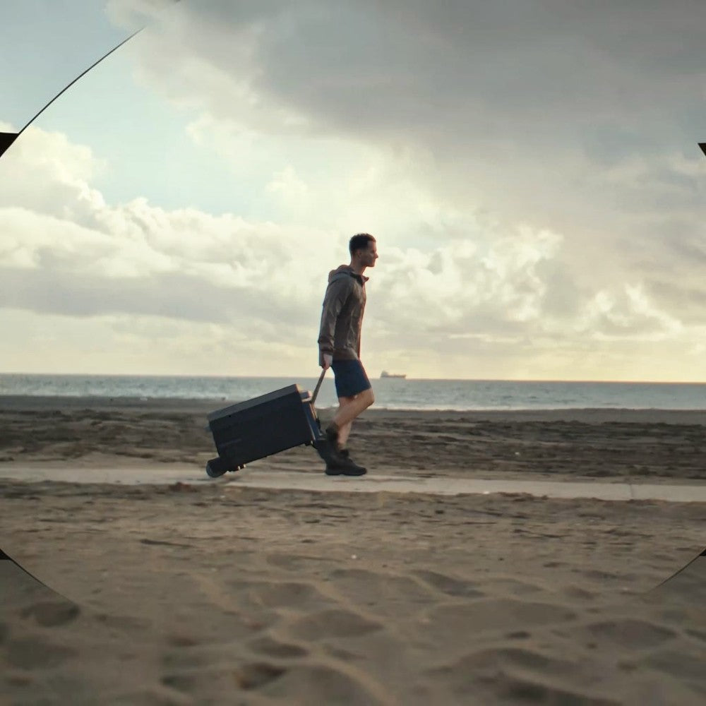 A man pulling an EcoFlow Glacier portable fridge on a beach using the detachable wheel and handle kit.